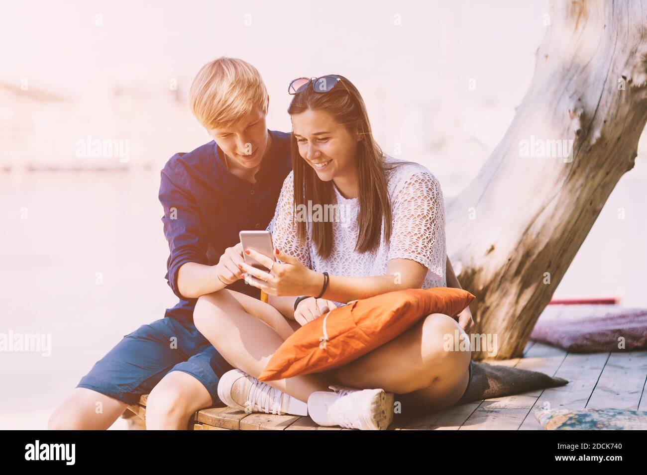 Young smiling white couple uses a smartphone on the beach in summer vacation Stock Photo