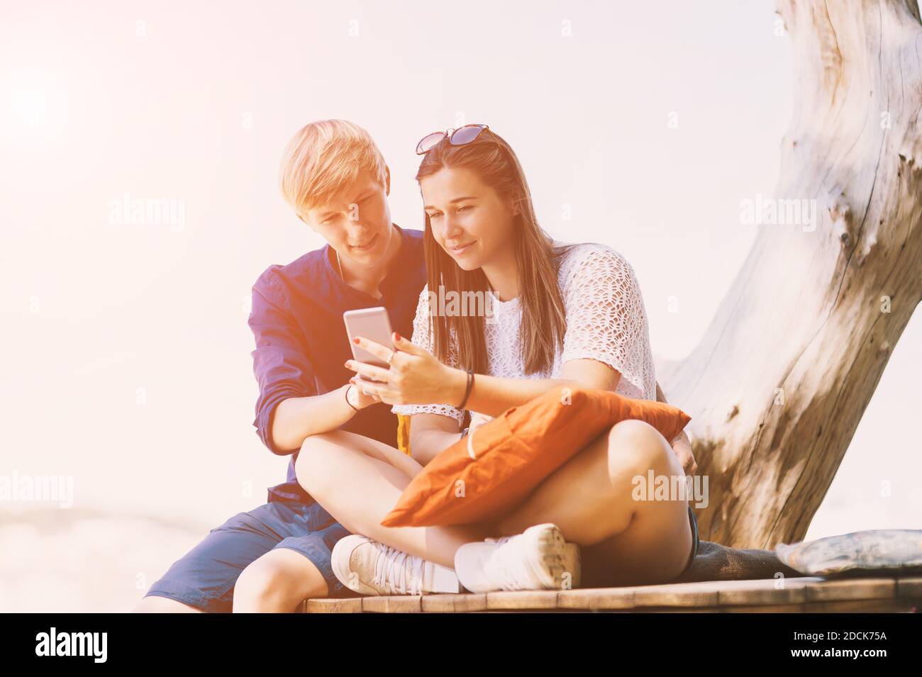 Young smiling white couple uses a smartphone on the beach in summer vacation Stock Photo