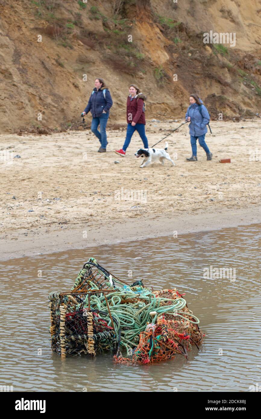 Pollution. Lost fishing gear. Overboard lobster pots, coloured plastic net. Lying in shallow water on Happisburgh beach. Background exercising dog wal Stock Photo
