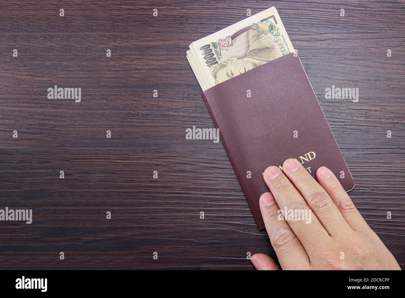 Man's hand holding an international passport and Japanese money on a brown dark wooden table. Stock Photo