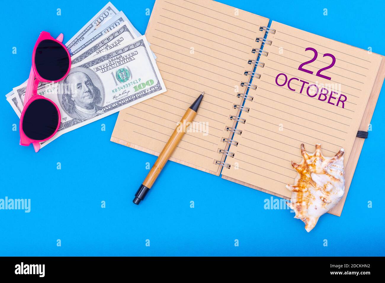 22 of October. October 22nd. Travel plan flat design with notepad written date, pen, glasses, money dollars and seashell on blue background. Autumn mo Stock Photo