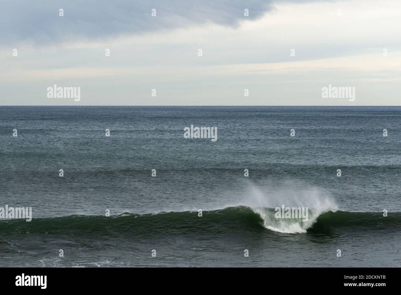 A large wave breaking in the ocean with copy space and blue and cloudy ...