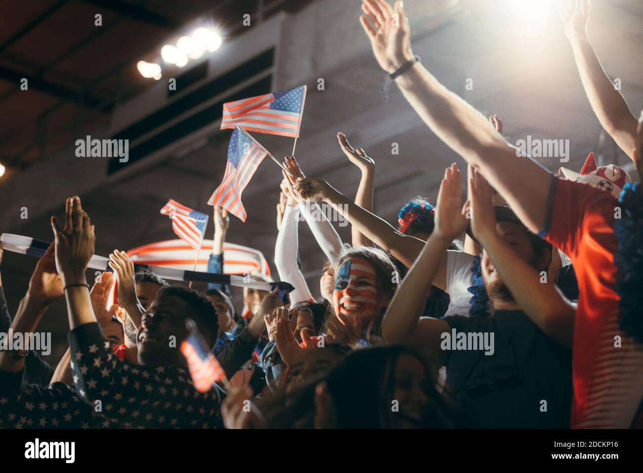 Soccer fans in stadium with face painted in USA flag colors and waving