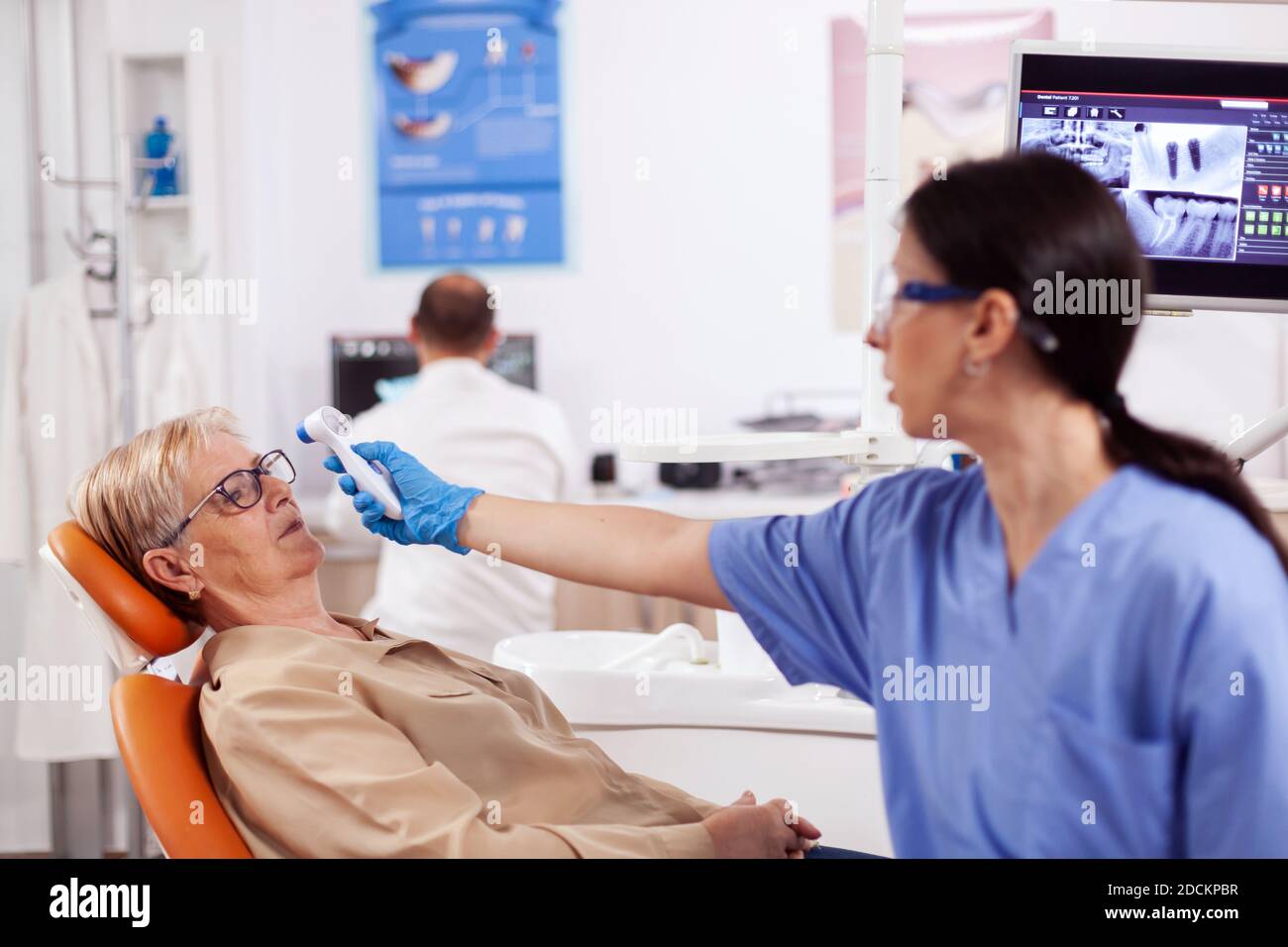 Dentist assistant measuring senior woman body temperature using