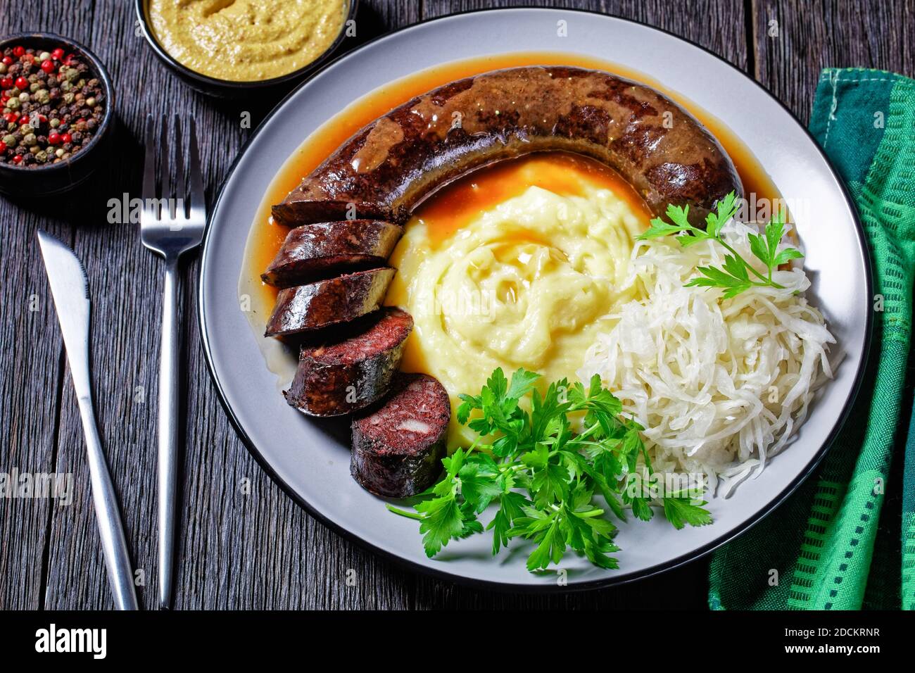 German food: blutwurst or blood sausage served on a plate with sauerkraut, mashed potato parsley, mustard, and peppercorns on a dark wooden table, top Stock Photo