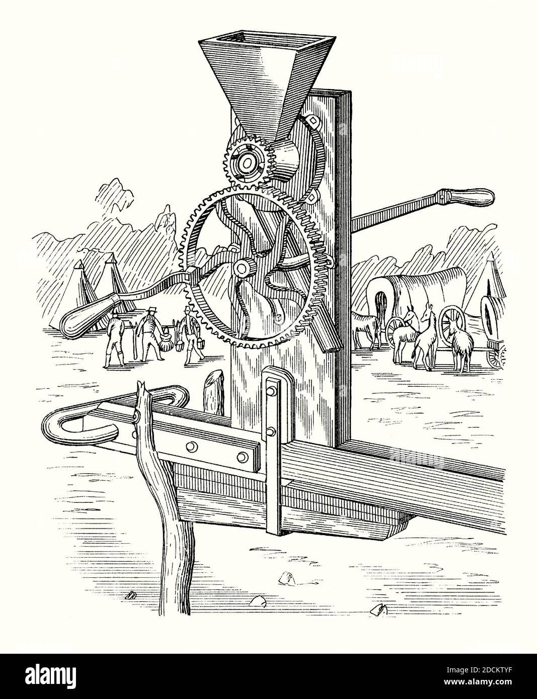 An old engraving of an ‘emigrant mill’, designed to be used by American pioneer settlers on the trails west. It is from a Victorian mechanical engineering book of the 1880s. The hand-operated mill was clamped to a waggon. The waggon train and tents at a campsite are seen in the background. A mill is a device that breaks solid materials into smaller pieces by grinding, crushing, or cutting. Stock Photo
