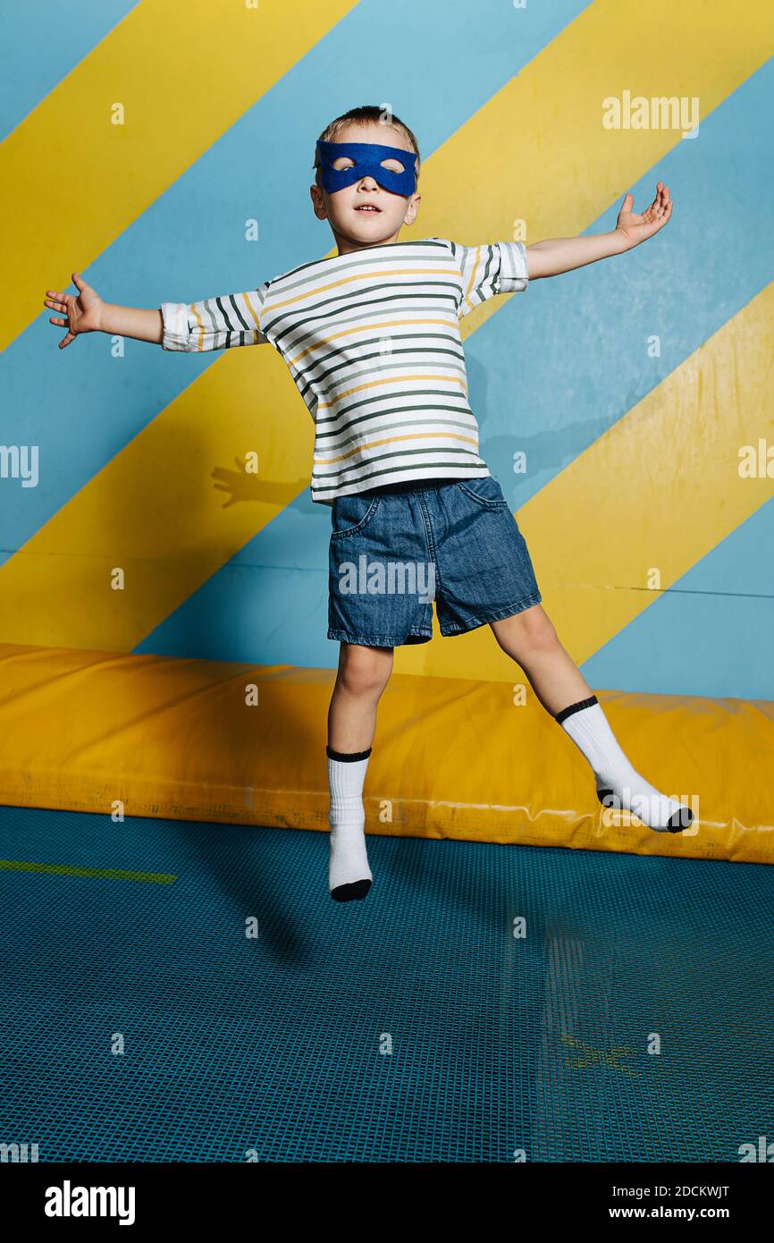 Awkward funny cute boy in mask jumping on trampoline in entertainment