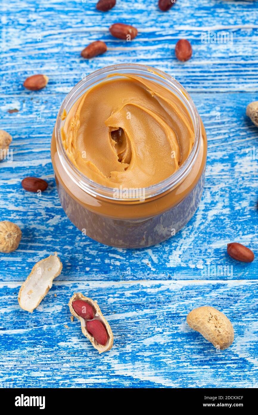 Peanut butter in an open jar and peanuts in the skin are scattered on