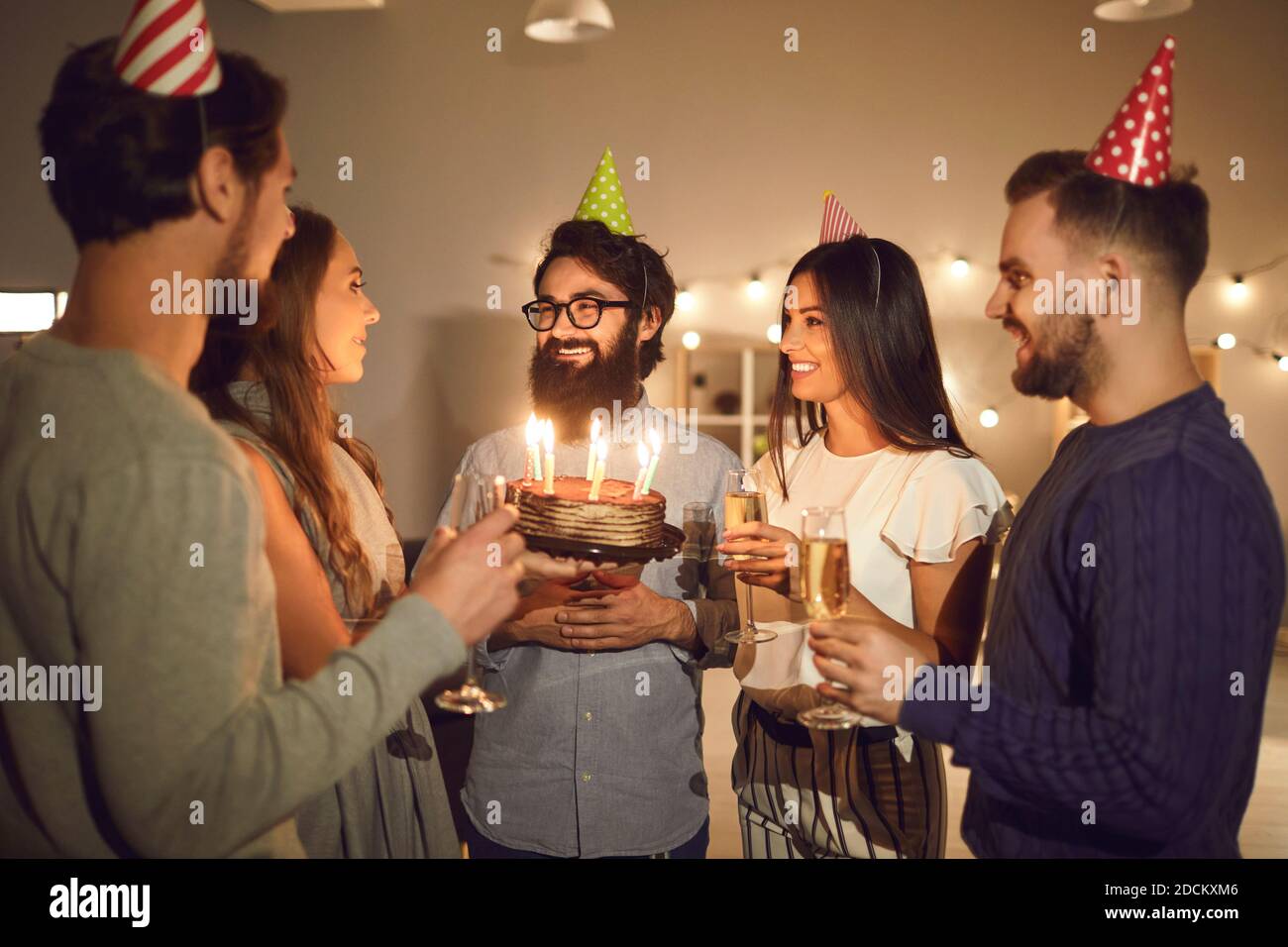 Group of people in cone party hats congratulate on the birthday of their happy friend. Stock Photo