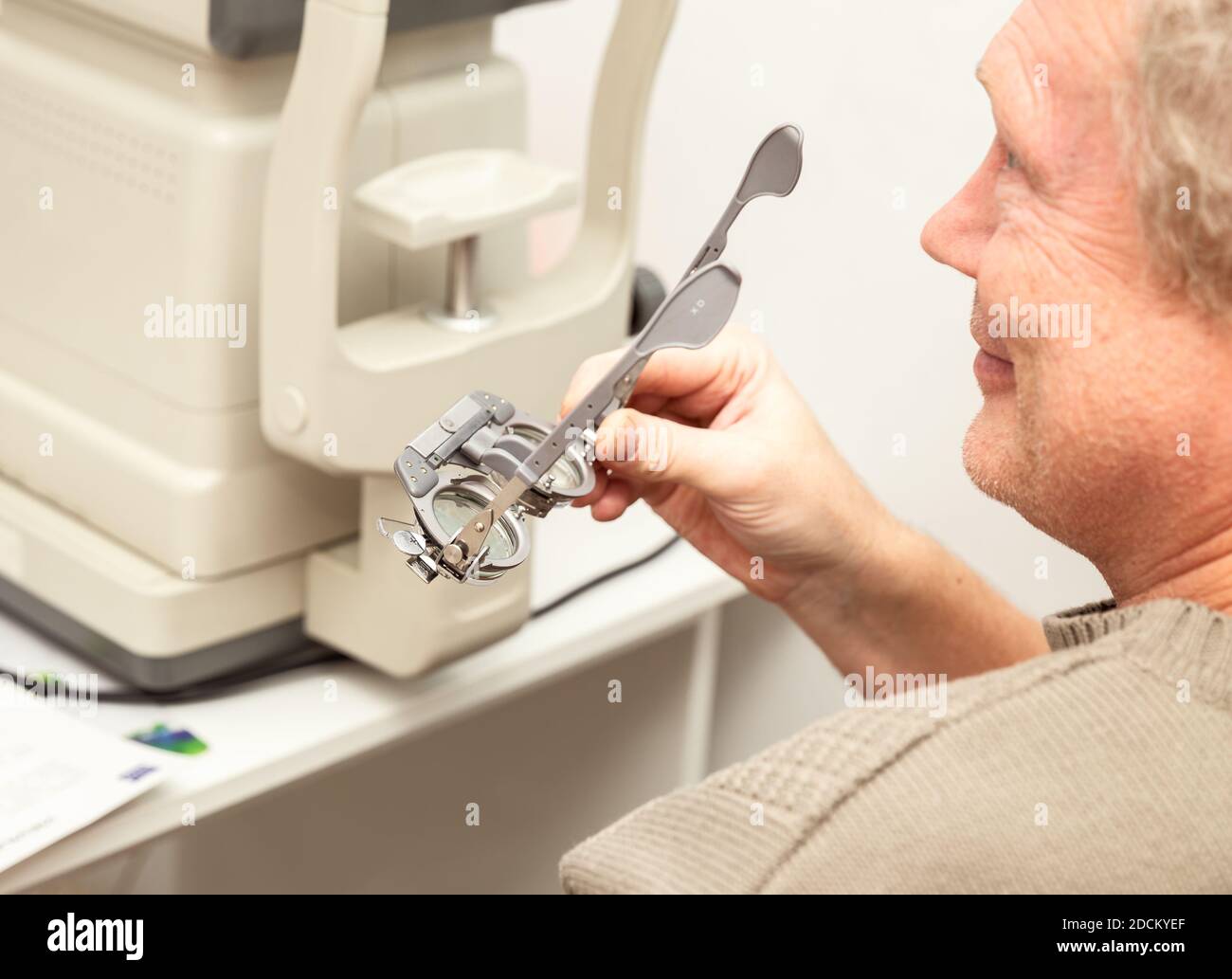 Senior man holding optometric trial frame for the selection of diopters. Ophthalmological clinic, vision examination. Stock Photo