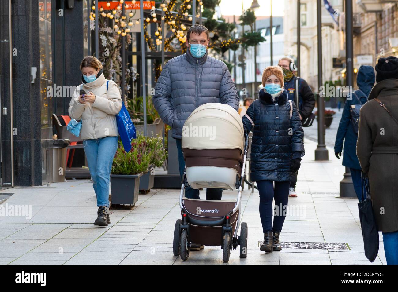 Couple with stroller and people wearing protective face masks walking in the city near a shop or shopping center during Christmas, Covid or Corona Stock Photo