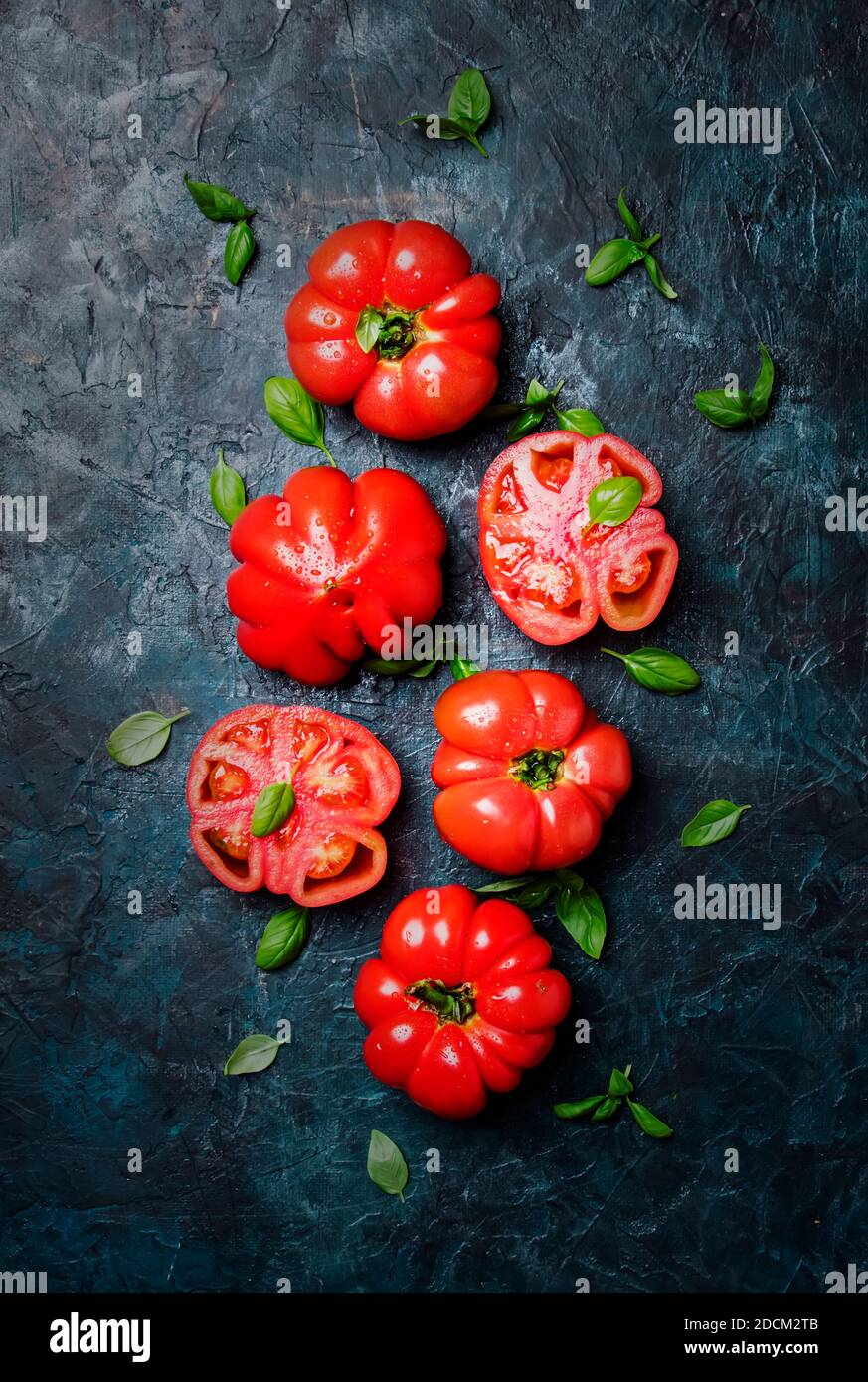 Big red tomatoes with green basil leaves on the old stone table, top ...
