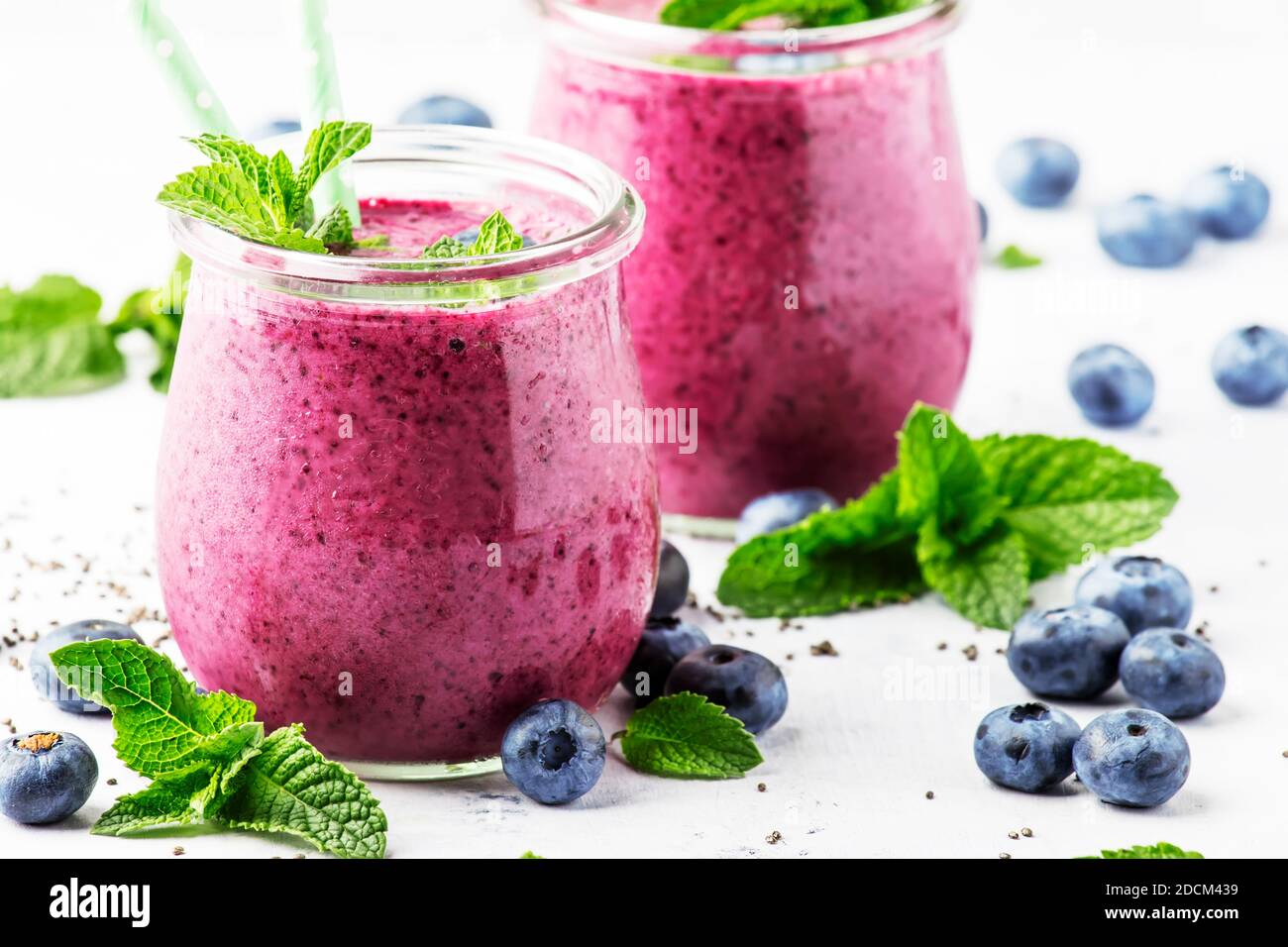 Purple homemade yogurt or smoothie with blueberries, chia seeds and mint leaves in glass jars on gray background, selective focus Stock Photo