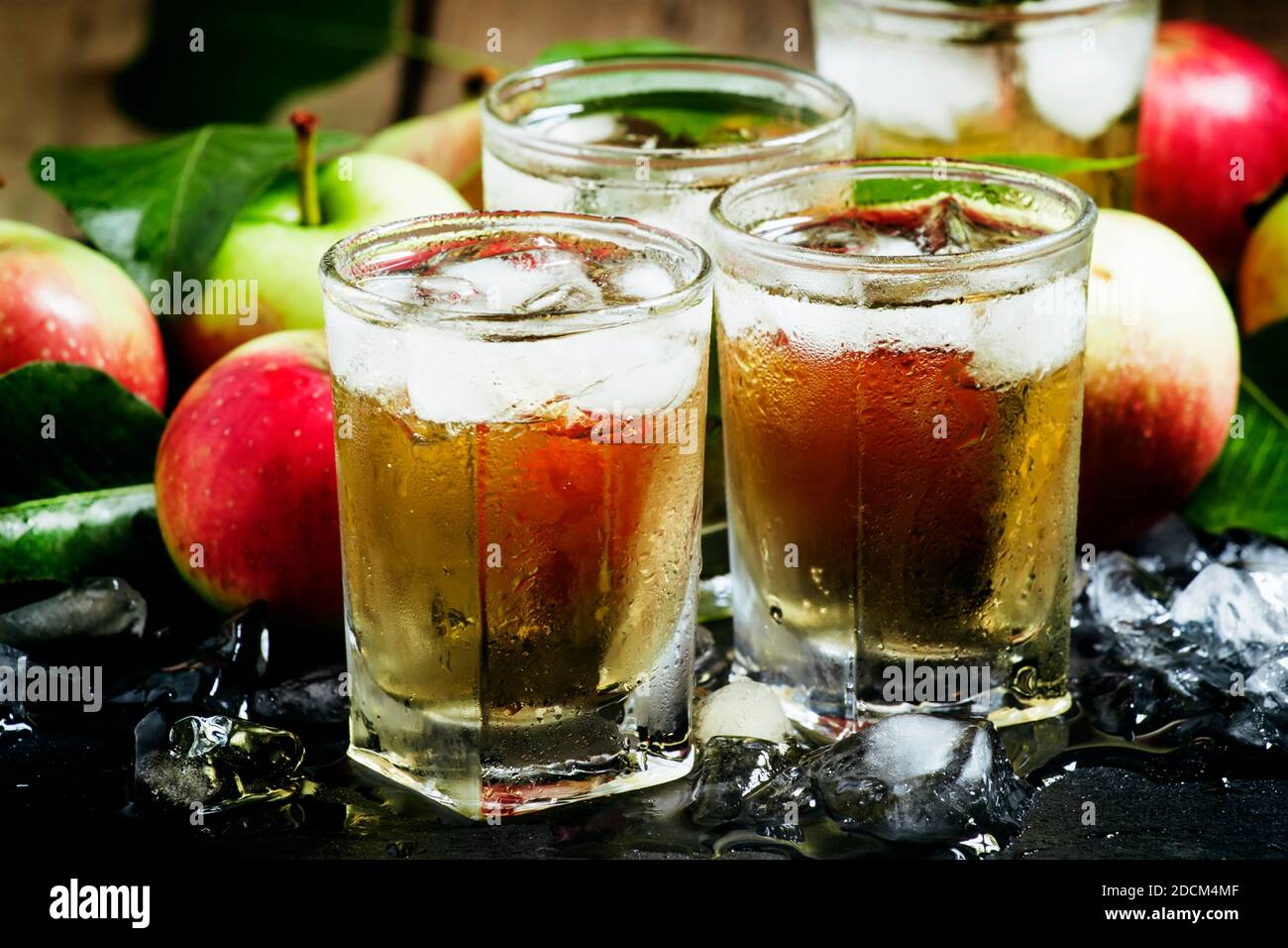 Cold apple juice with crushed ice, fresh apples with green leaves on a dark background, selective focus Stock Photo