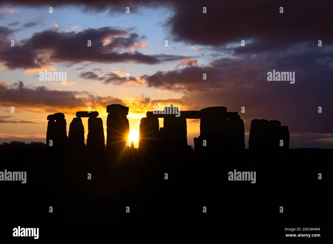 A dramatic sunset illuminates a cloudy sky over the silhouettes of the standing stones at Stonehenge, Wiltshire, England. Stock Photo