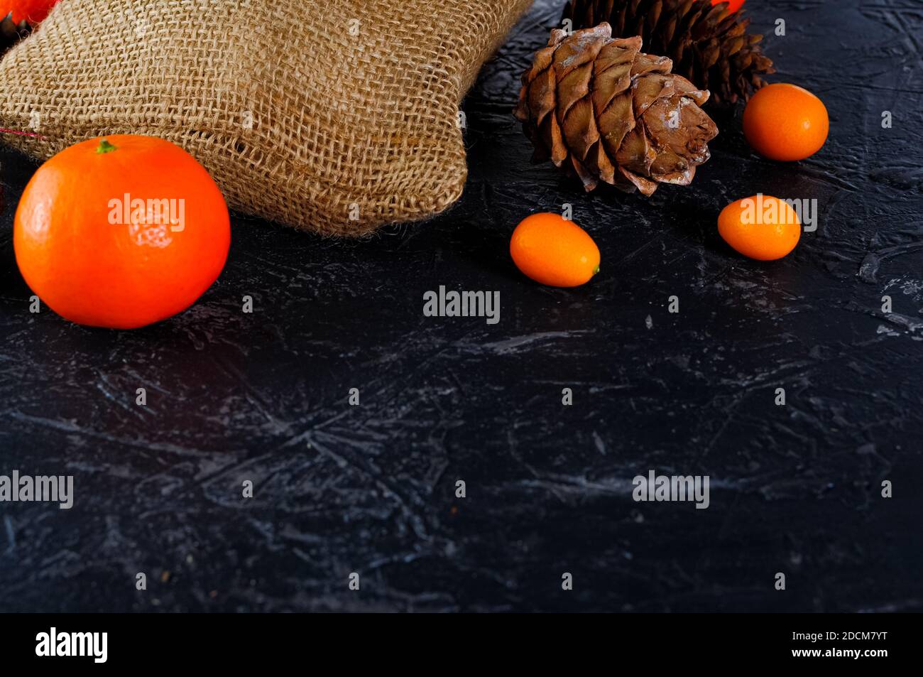 Christmas bag made of coarse burlap, cones, tangerines or oranges, kumquat on a dark background. Copy space. Stock Photo