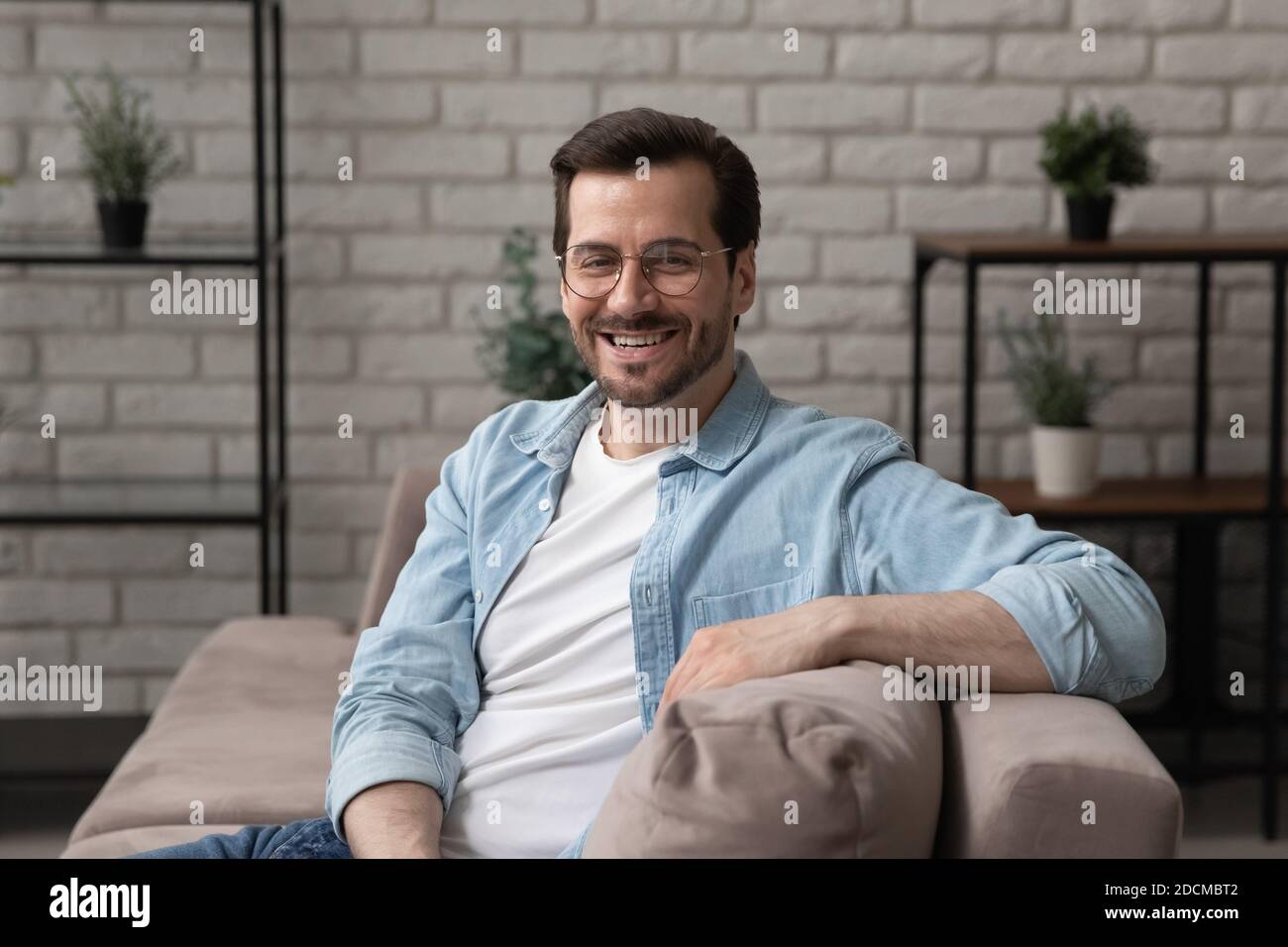 Portrait of smiling young 30s handsome man sitting on sofa. Stock Photo