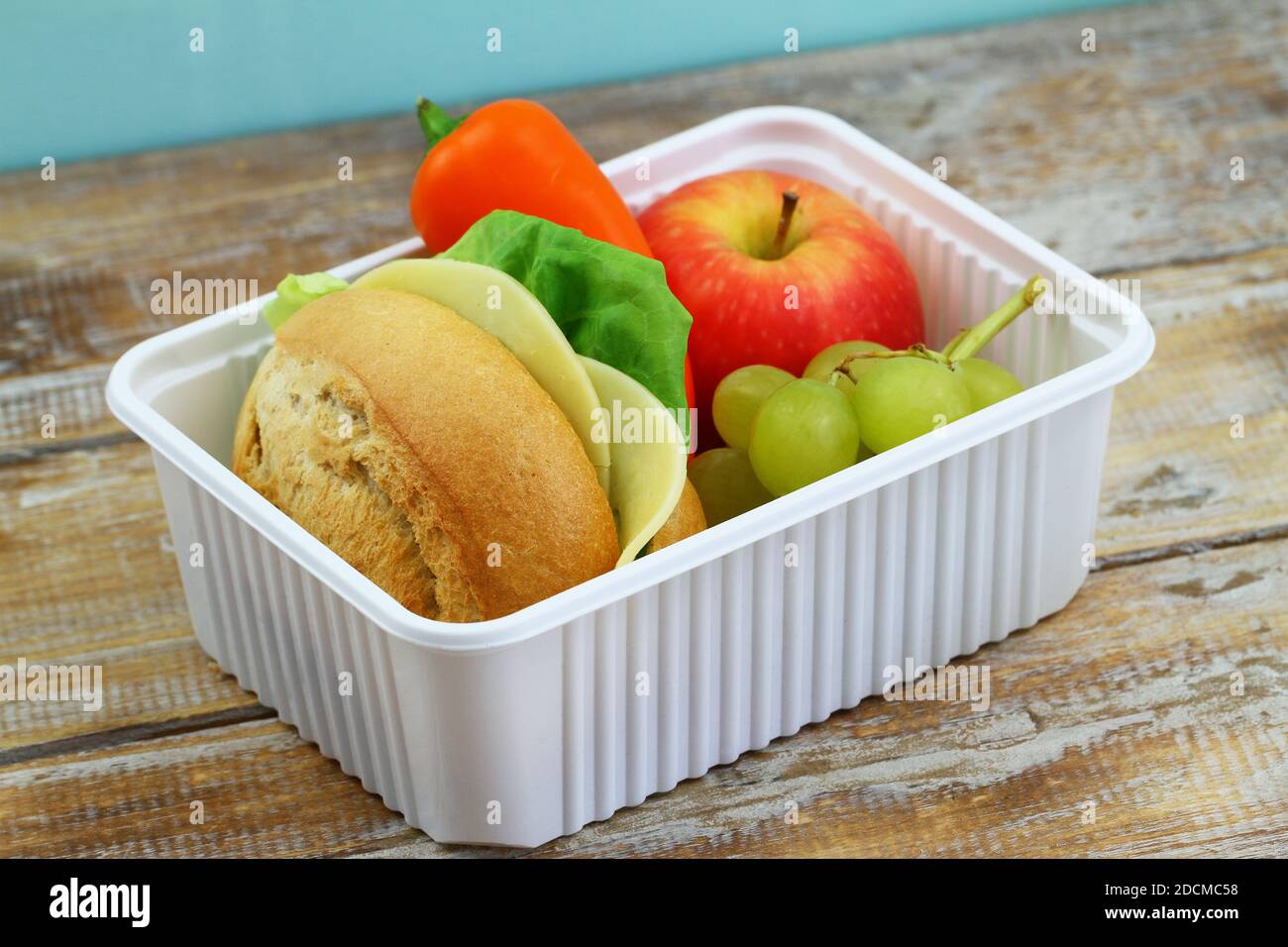 Nutritious packed lunchbox containing brown cheese sandwich, crunchy yellow pepper and fresh fruit in white plastic box Stock Photo