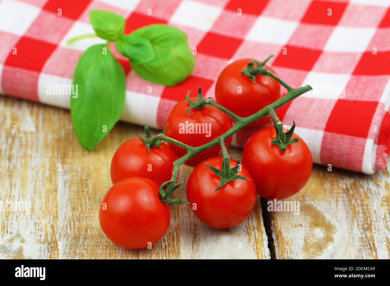 Fresh cherry tomatoes and fresh basil leaves on red and white checkered ...