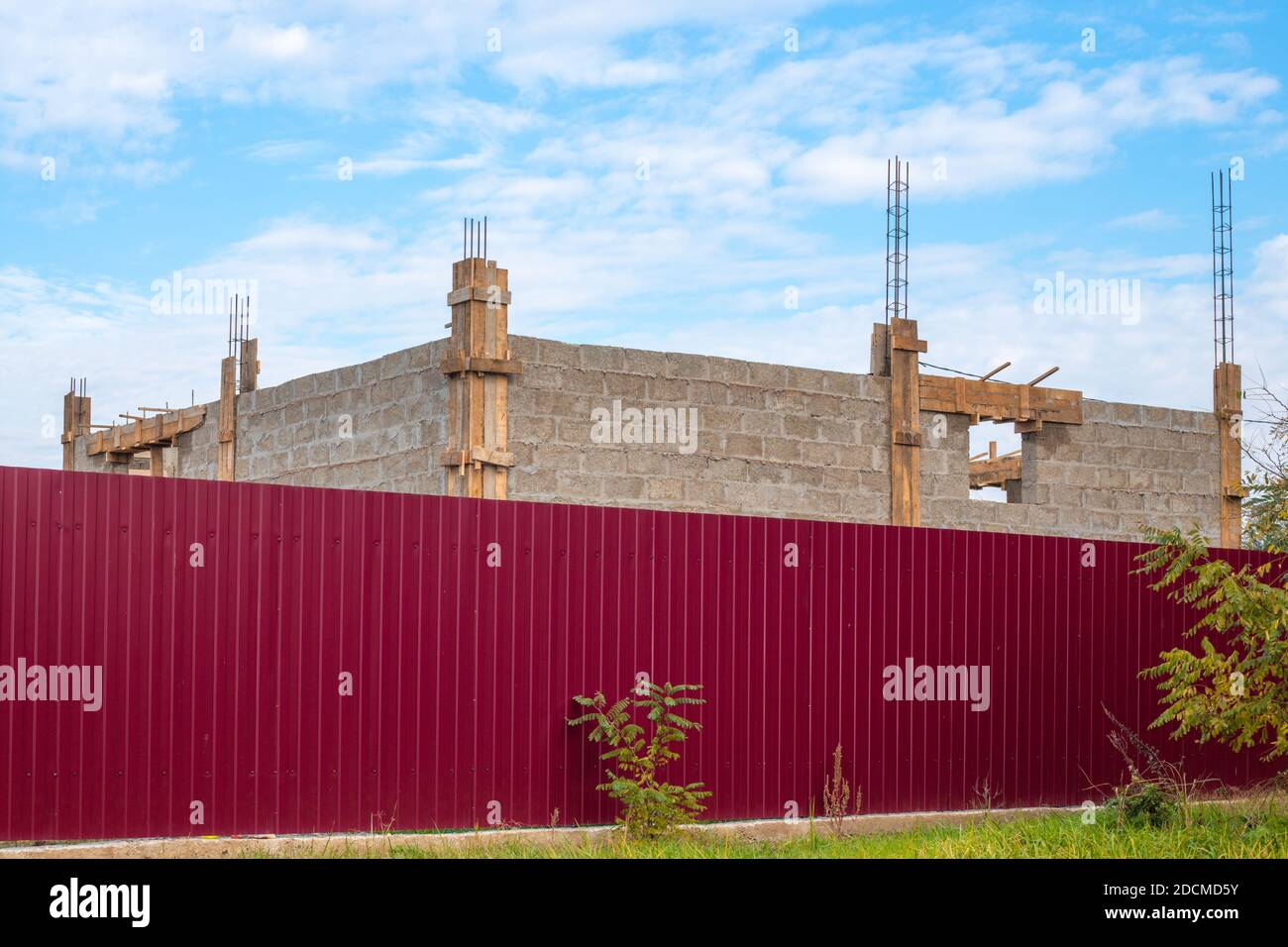 Construction stages. Cinder block house with protruding fittings behind a burgundy fence. Stock Photo