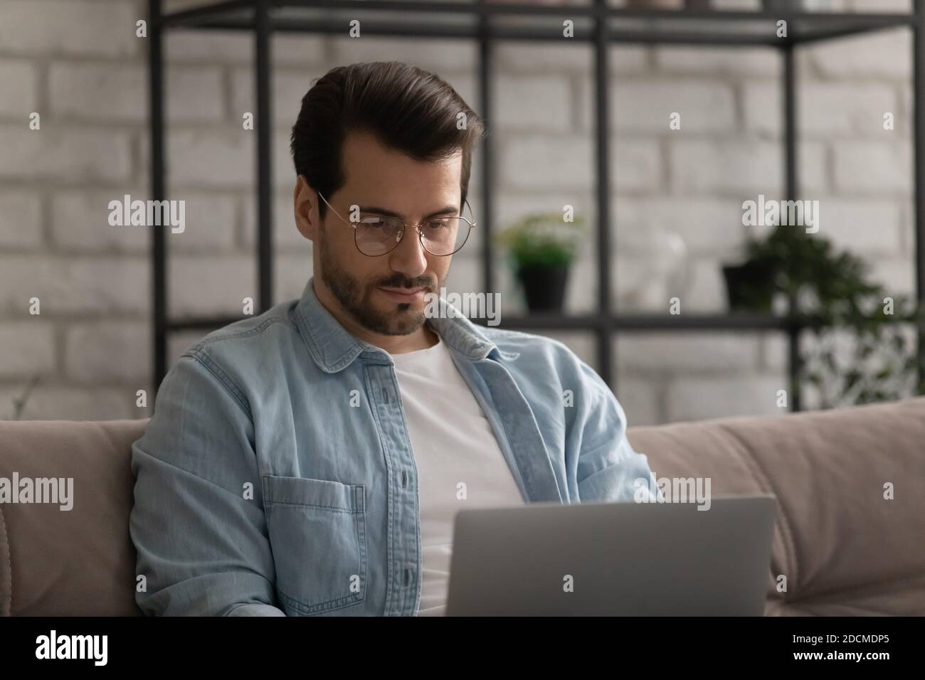 Focused young man in glasses working distantly on computer Stock Photo