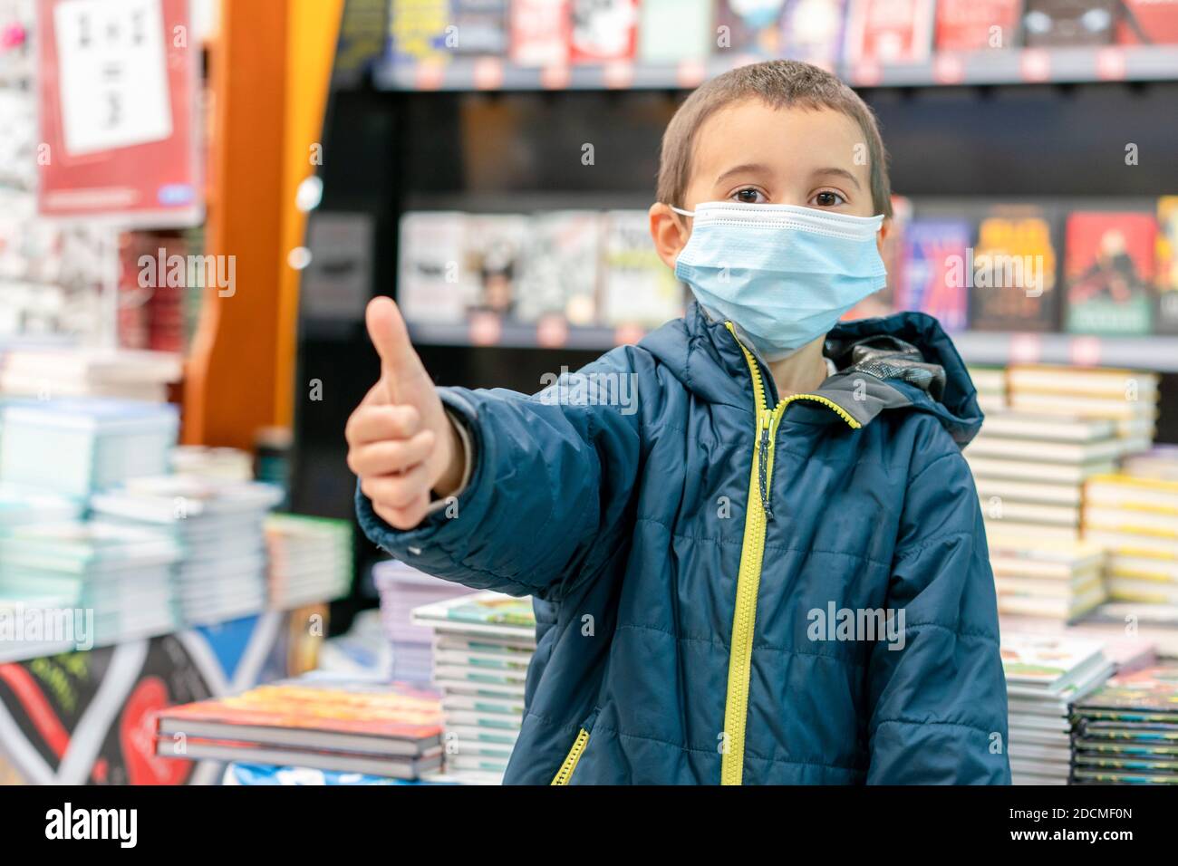 Boy in medical mask at bookstore. young boy chooses books in a bookshop. boy wear a protective mask In a bookstore. Concept of life And protect Stock Photo
