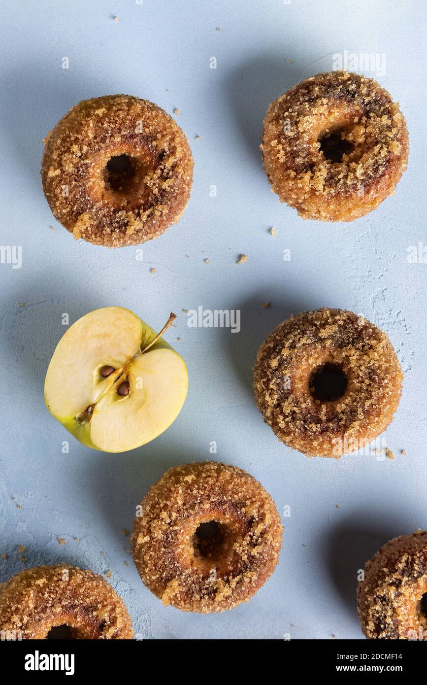 Close-up of homemade baked sugared apple cider donuts and cut apple on blue textured surface. Ready to eat snack. Small batch food with ingredient. Di Stock Photo