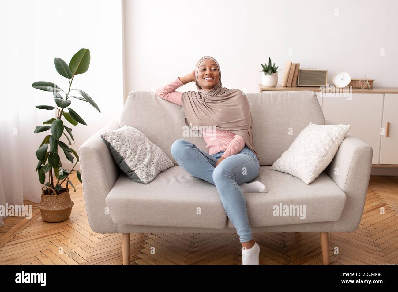 Full length portrait of black woman in hijab resting on comfy couch at ...