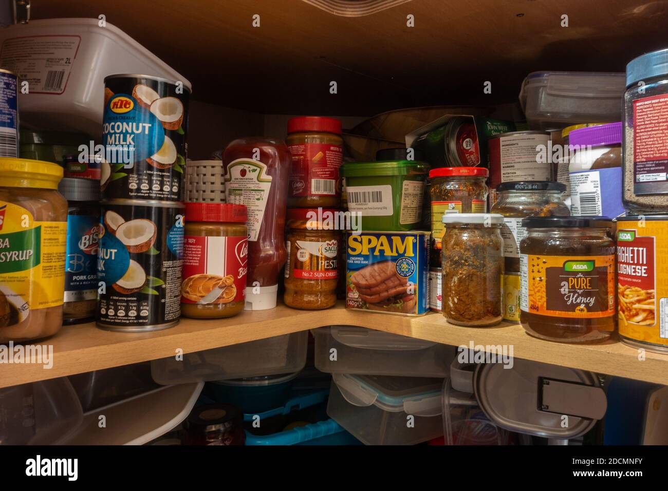 Bottles, jars and cans of food stored in a corner kitchen cupboard beneath the worktop. Stock Photo