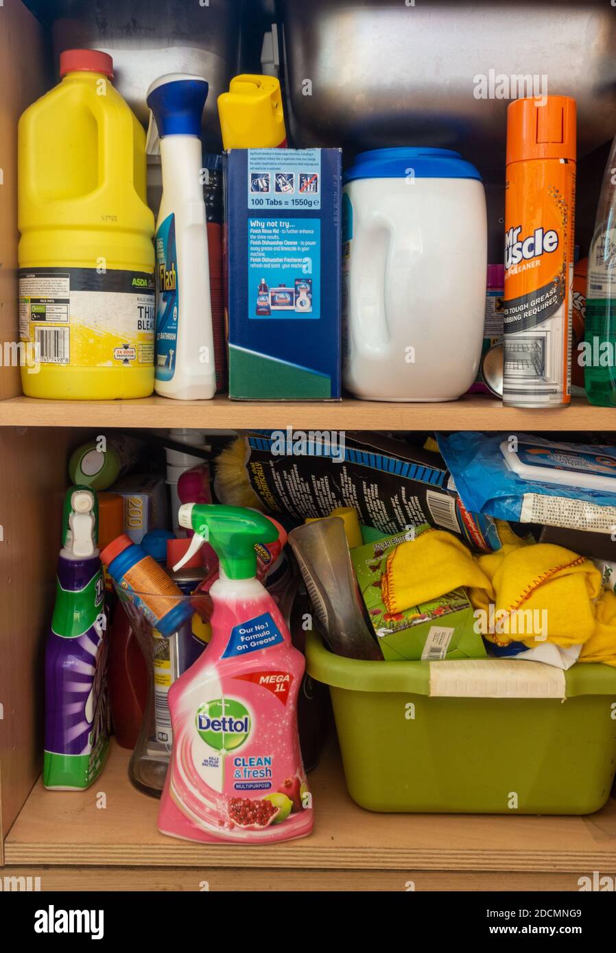 Cleaning products like bleach and antibacterial sprays in plastic bottles stored on shelves in the cupboard underneath the kitchen sink. Stock Photo