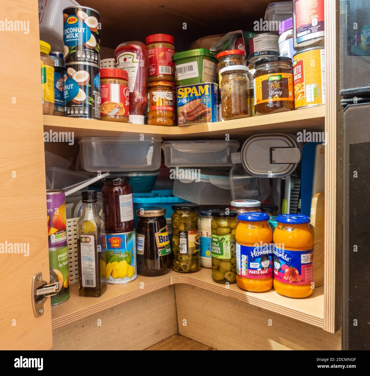 Bottles, jars and cans of food stored in a corner kitchen cupboard beneath the worktop. Stock Photo