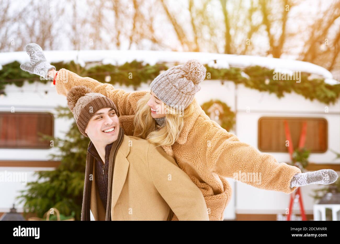 Cheerful millennial couple having fun outside at winter camping, woman piggybacking boyfriend Stock Photo