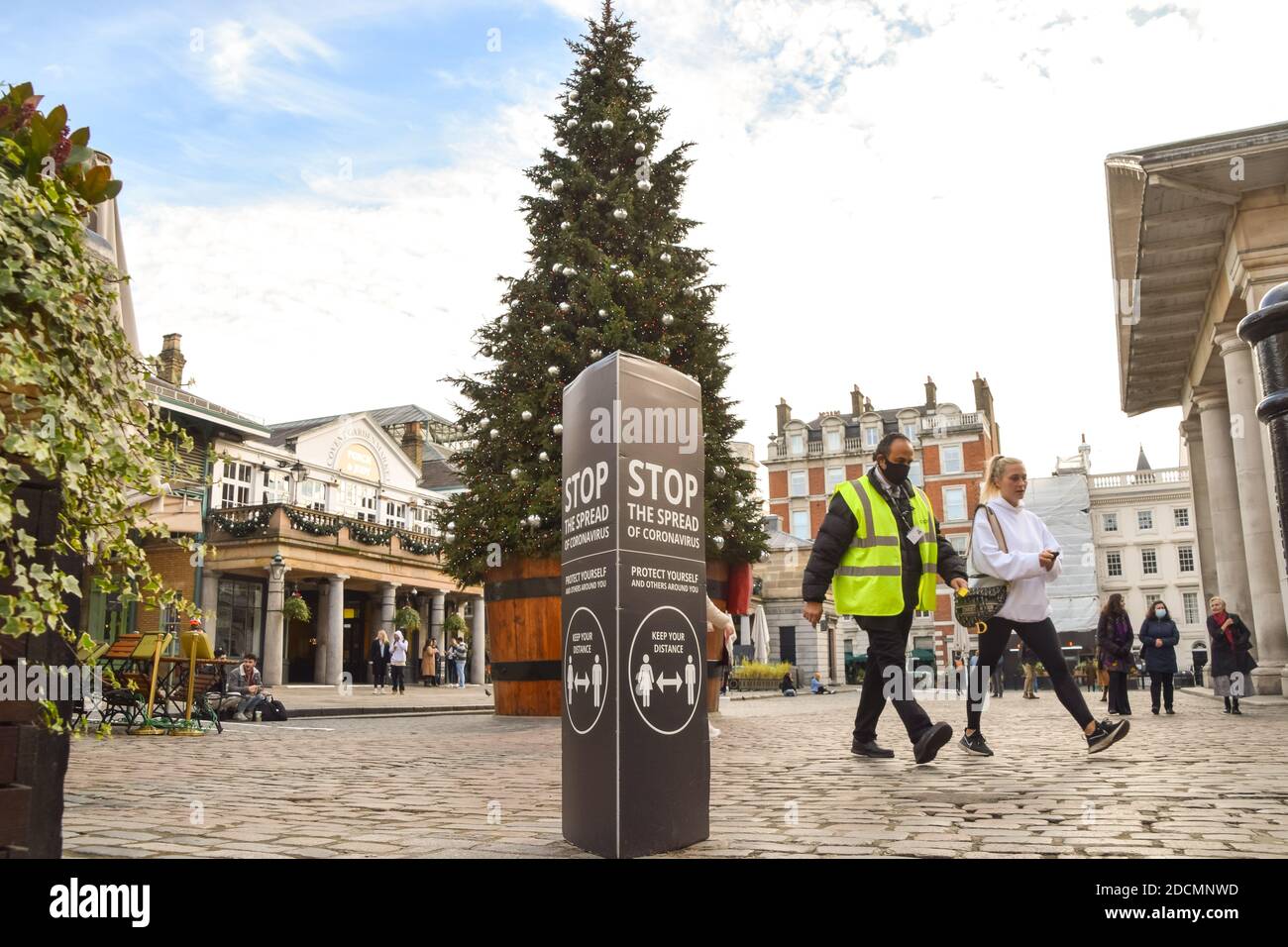 People walk past a Stop The Spread Of Coronavirus sign next to the Christmas Tree in Covent Garden, London. England is set to enforce a tough tier system once the lockdown ends on 2 December. Stock Photo