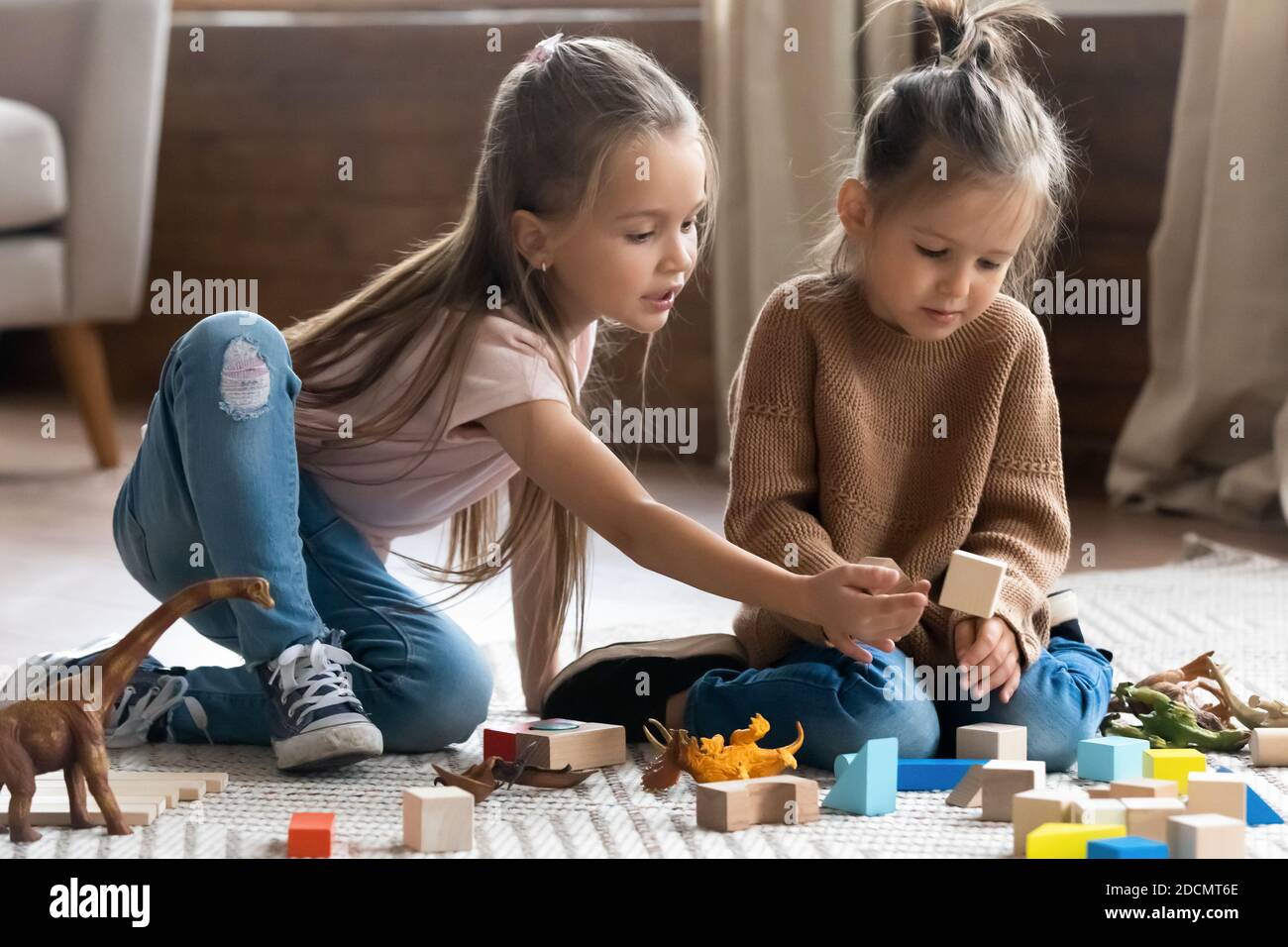 Two sisters play together wooden brick and dinosaurs toys set Stock Photo