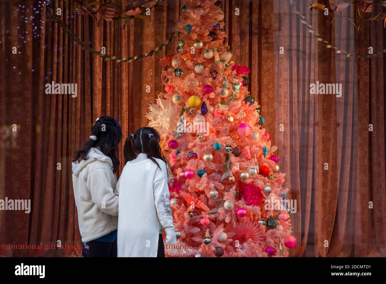 London, UK. 22 November 2020. Women view a Christmas tree in the window of  Selfridges department store on Oxford Street. The UK government is due to  ease certain coronavirus pandemic lockdown restrictions