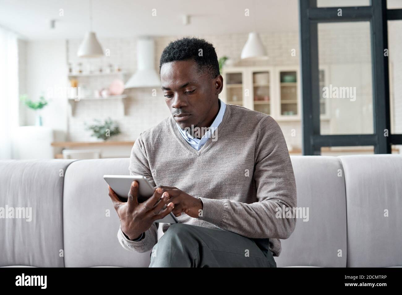 Serious african man using digital tablet apps sitting on couch at home. Stock Photo