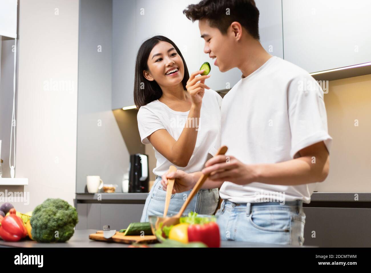 Japanese Couple Tasting Food While Cooking Dinner Together In Kitchen Stock Photo