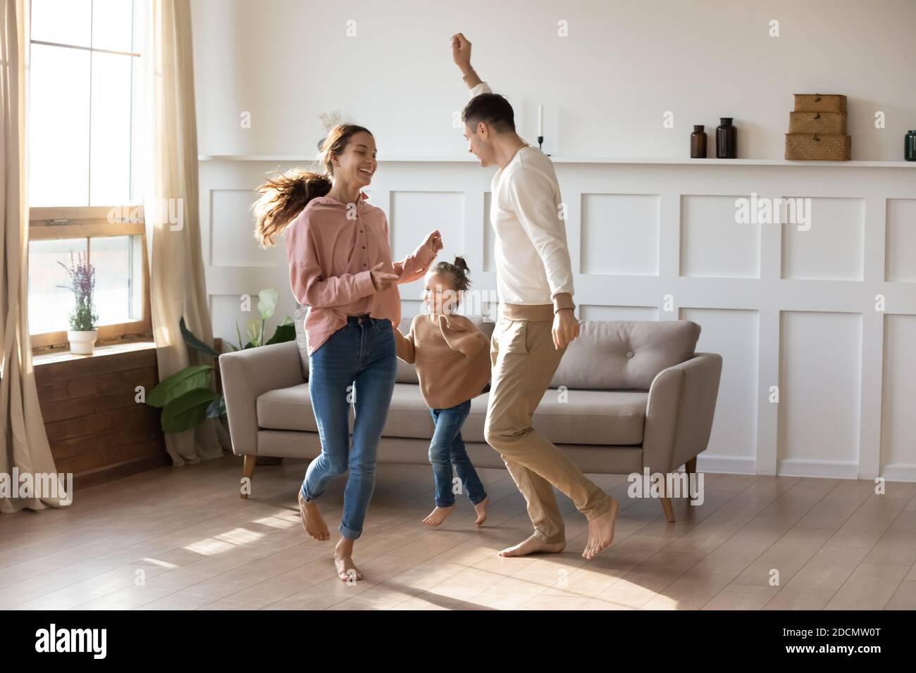 Couple dancing with little daughter barefoot in warm living room Stock Photo