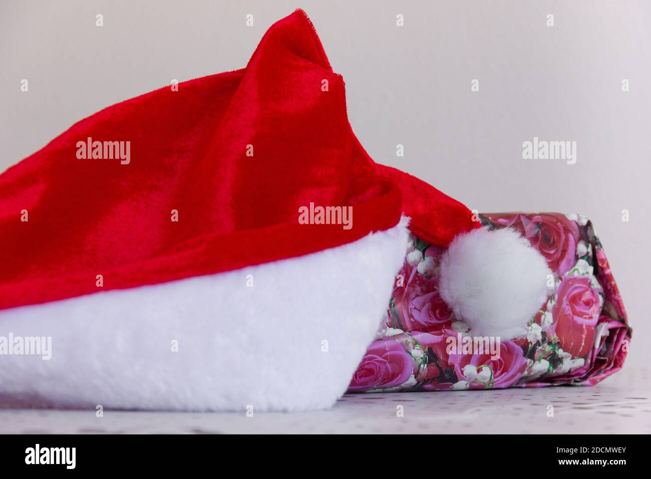 Santa red hat by gift with floral wrap. Christmas holiday season present, invisible friend, generosity concepts Stock Photo