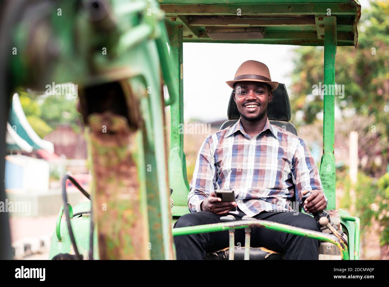 African worker driving heavy construction equipment backhoe with using smartphone Stock Photo