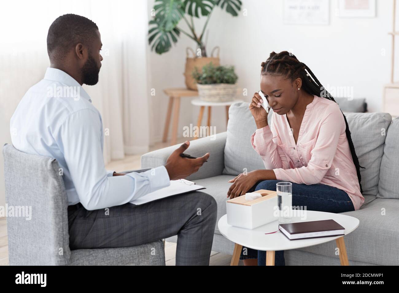 Black Psychologist Talking To Crying Woman During Therapy Session At His Office Stock Photo