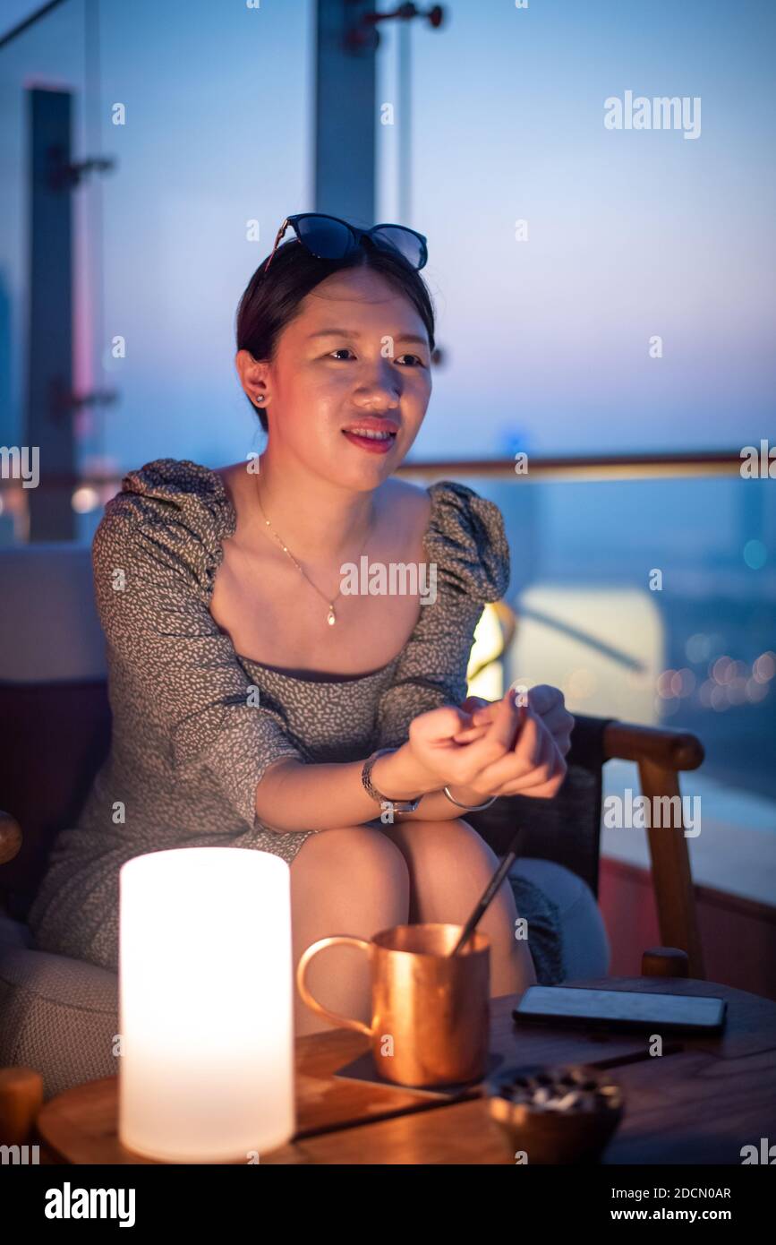 Woman having a drink with the Dubai city view in the United Arab Emirates from above at dusk Stock Photo