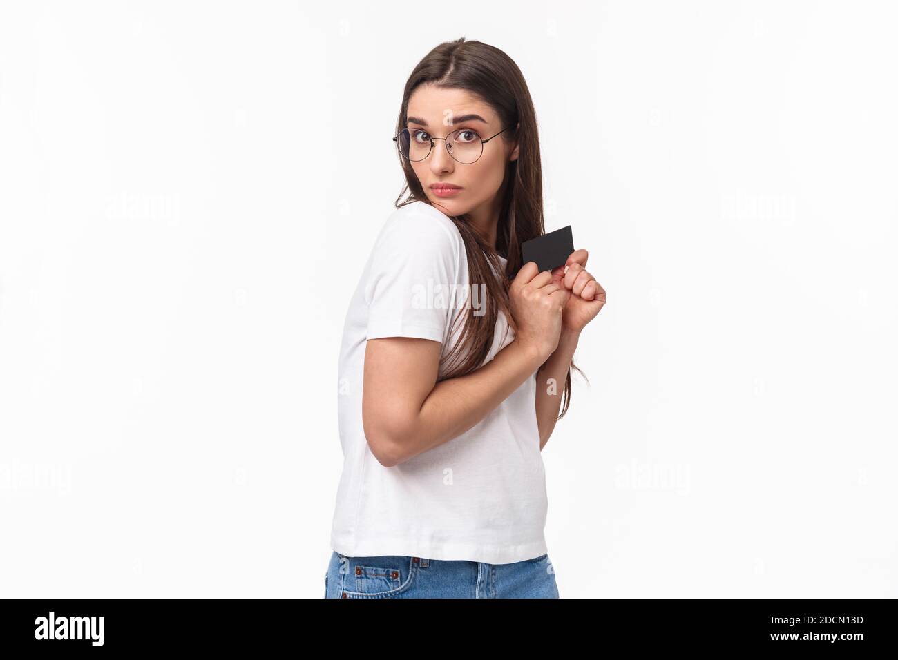 Portrait of greedy and funny young woman unwilling to give her credit card, hiding it and looking with disbelief and reluctance, have money but dont Stock Photo