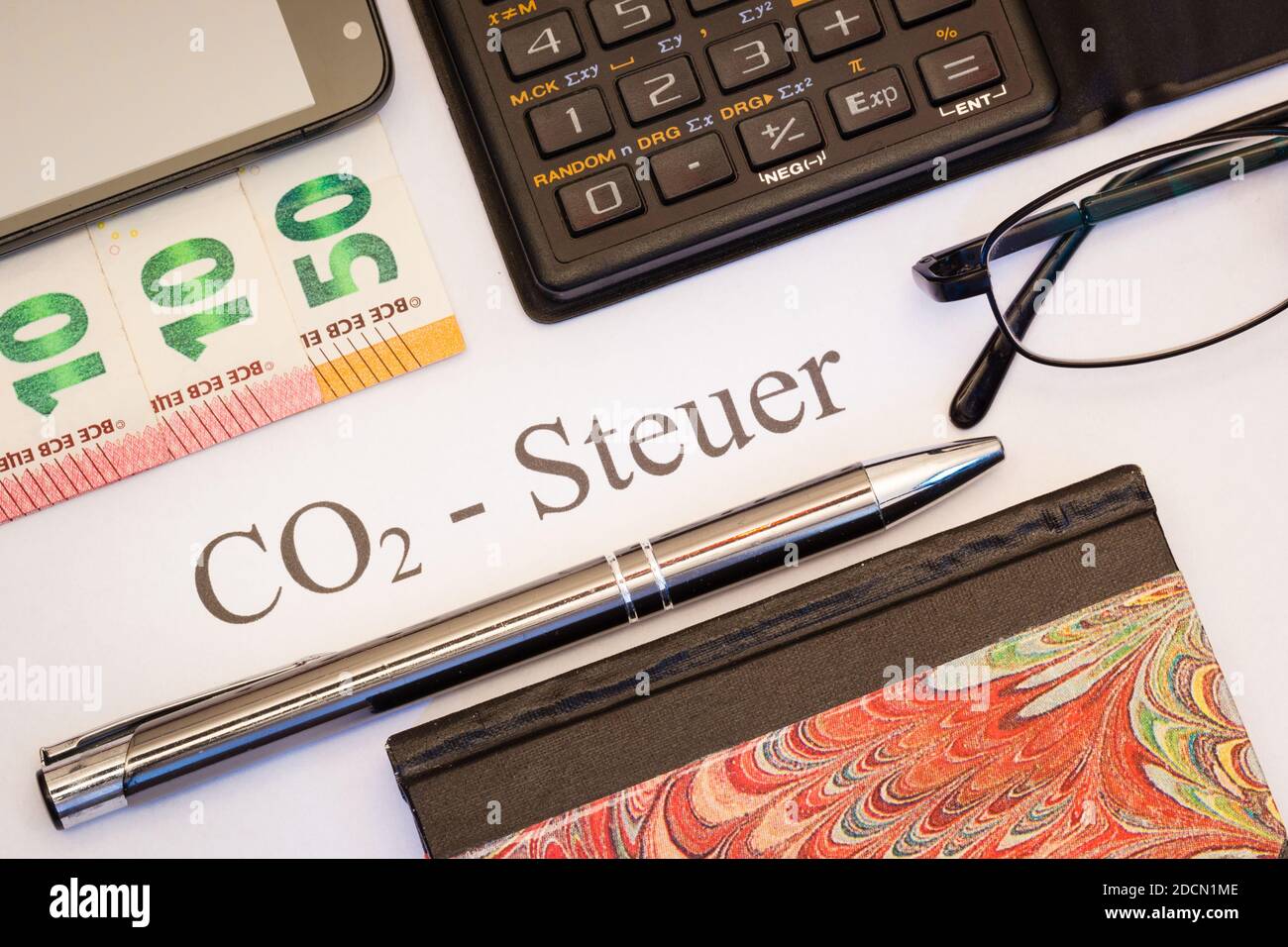 CO2-Steuer auf Papier zwischen Kugelschreiber, Euro Banknoten, Taschenrechner, Notizbuch und Smartphone Stock Photo