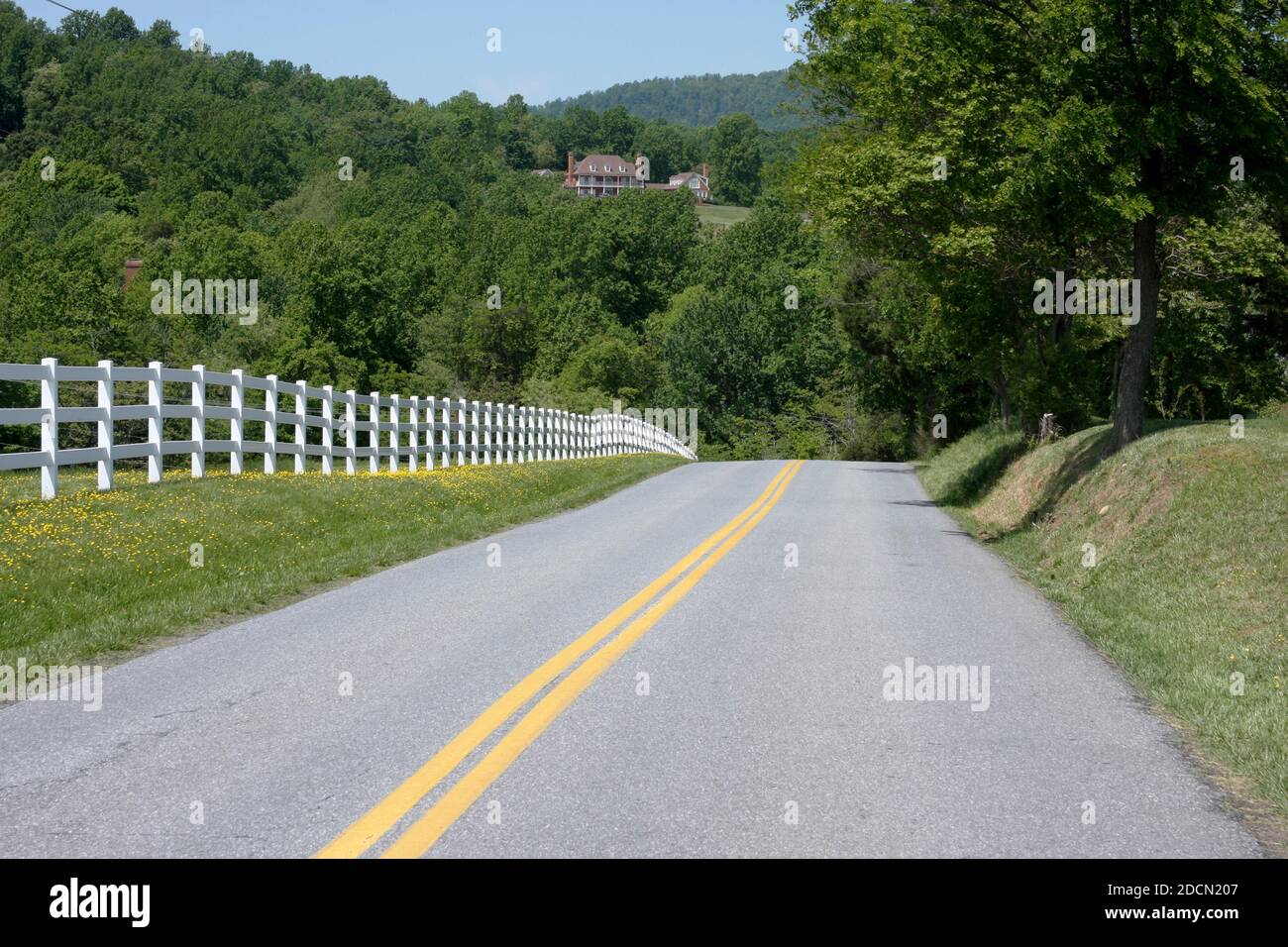 Two-lane country road in Virginia, USA. Rural property bordered by long vinyl fence, with view of the mountains. Stock Photo
