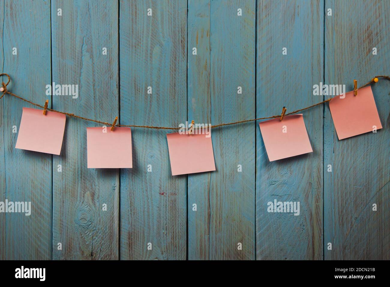 Pink note papers hanging on the rope against blue rustic wooden background. Copyspace. Concept of memo messages, to do list Stock Photo