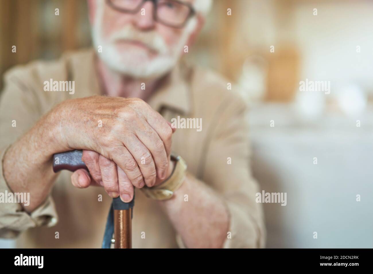 Cropped photo of senior bearded man resting at home and holding wooden walking stick. Focus on cane. Care and health concept Stock Photo