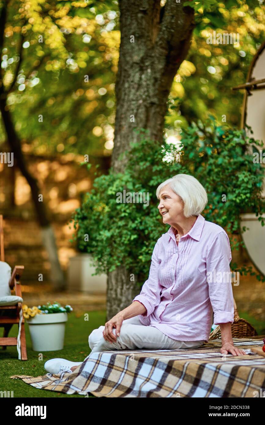 Side view of happy senior woman sitting on a blanket on the porch of the van. Lifestyle concept. Copy space Stock Photo