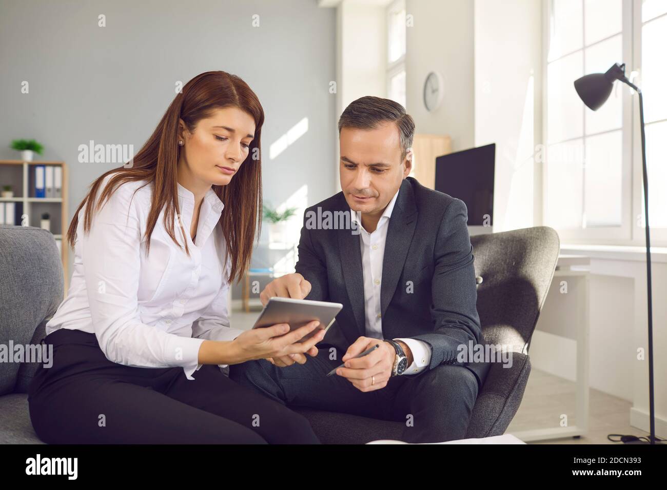 Male and female office workers sitting with a digital tablet and checking workflows in the office. Stock Photo