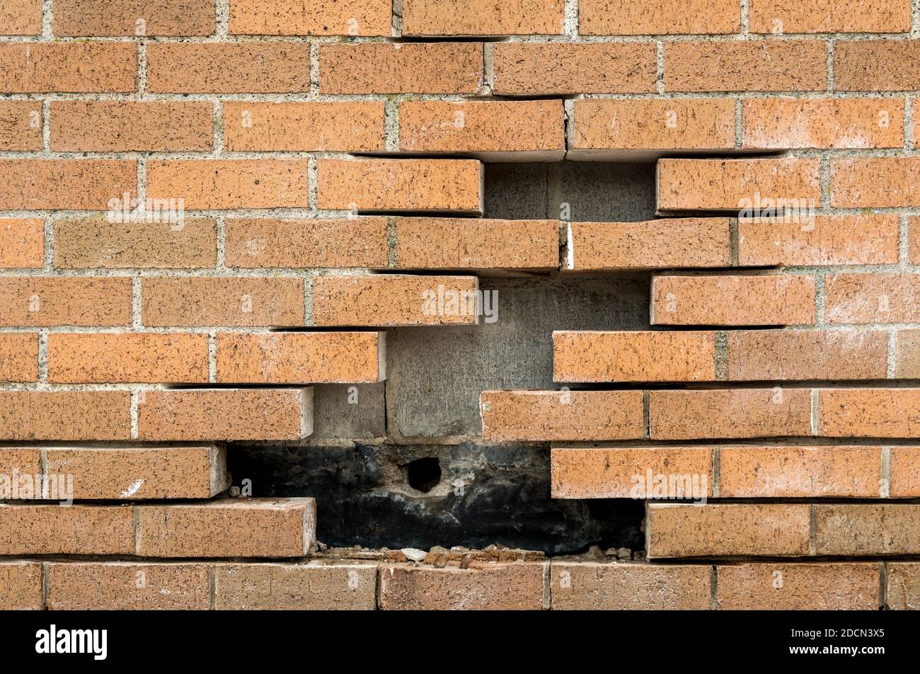 Bricks missing from a brick wall. Concrete blocks are behind the brick